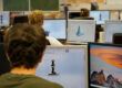 Ein junger Mann sitzt gemeinsam mit anderen Studierenden im Hörsaal einer Hochschule. Vor ihm steht ein Notebook.
